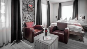 A modern hotel room with a stone accent wall, a bed with white bedding, leather armchairs, and a wooden coffee table.