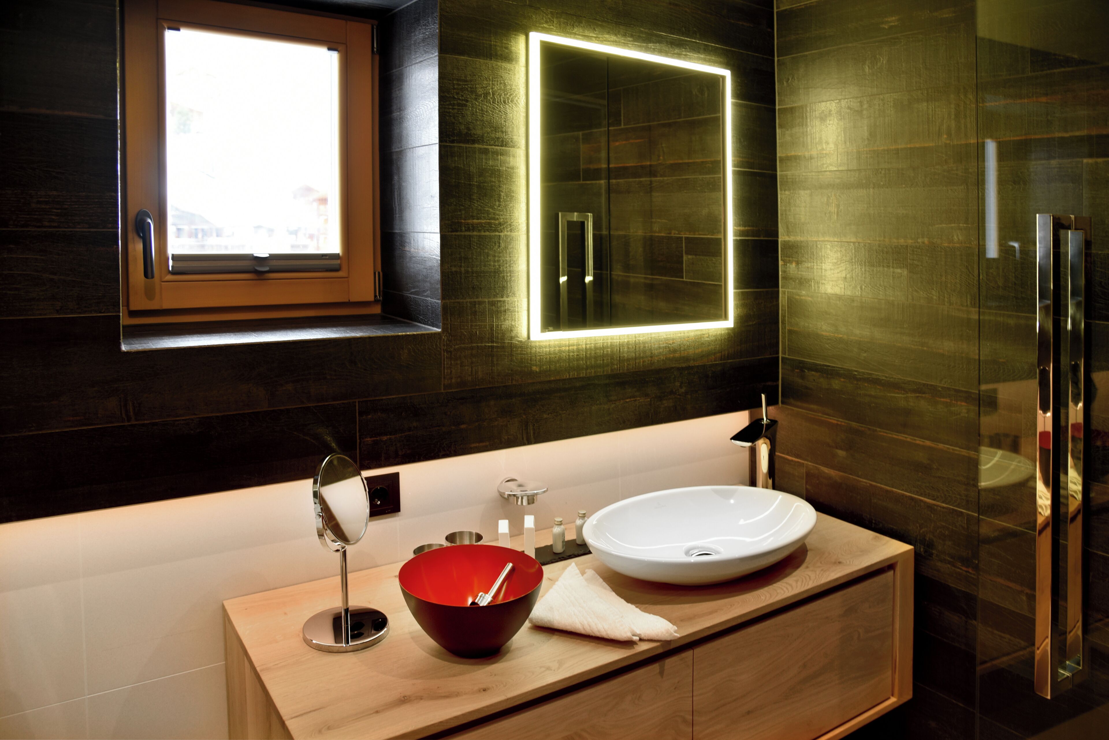 A modern bathroom with a wooden vanity, a round sink, and a large mirror.