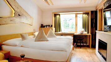 Une chambre d’hôtel avec un grand lit, une petite table, une chaise, une cheminée et une fenêtre avec des rideaux.