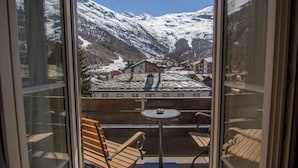 Un balcon avec une table et des chaises, d’où l’on peut admirer une montagne enneigée et un village.