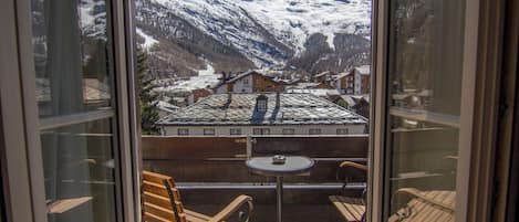 A balcony with a table and chairs, overlooking a snow-covered mountain and a village.