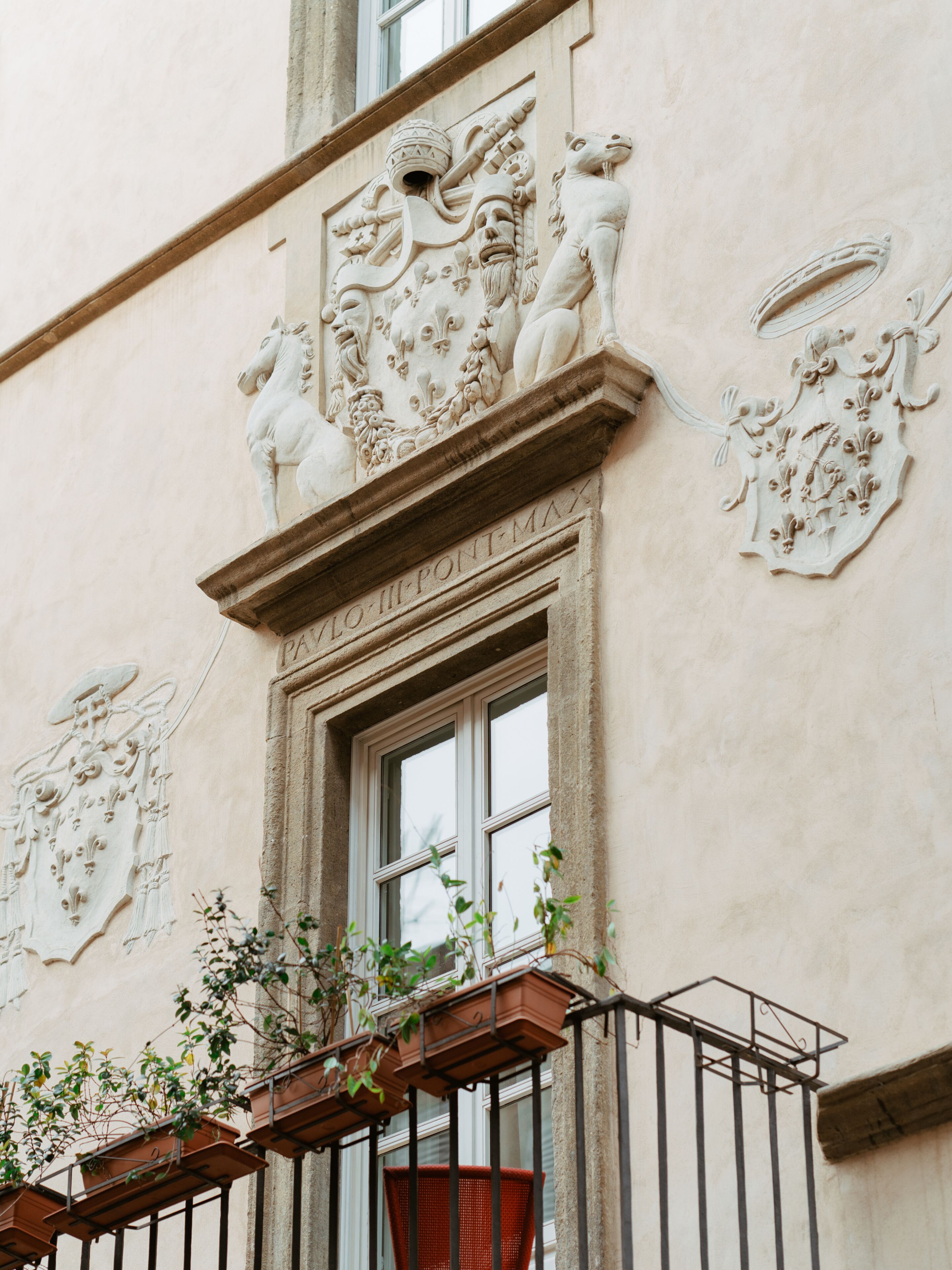 A building facade with ornate stone carvings, including a coat of arms and a window with a balcony.