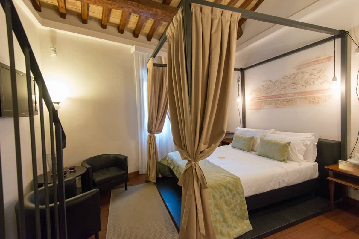 A bedroom with a four-poster bed, a desk, a chair, and a staircase.