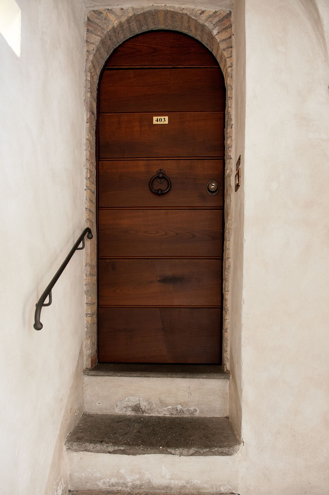 A wooden door with a number plate, a metal handle, and a metal hook on the wall.