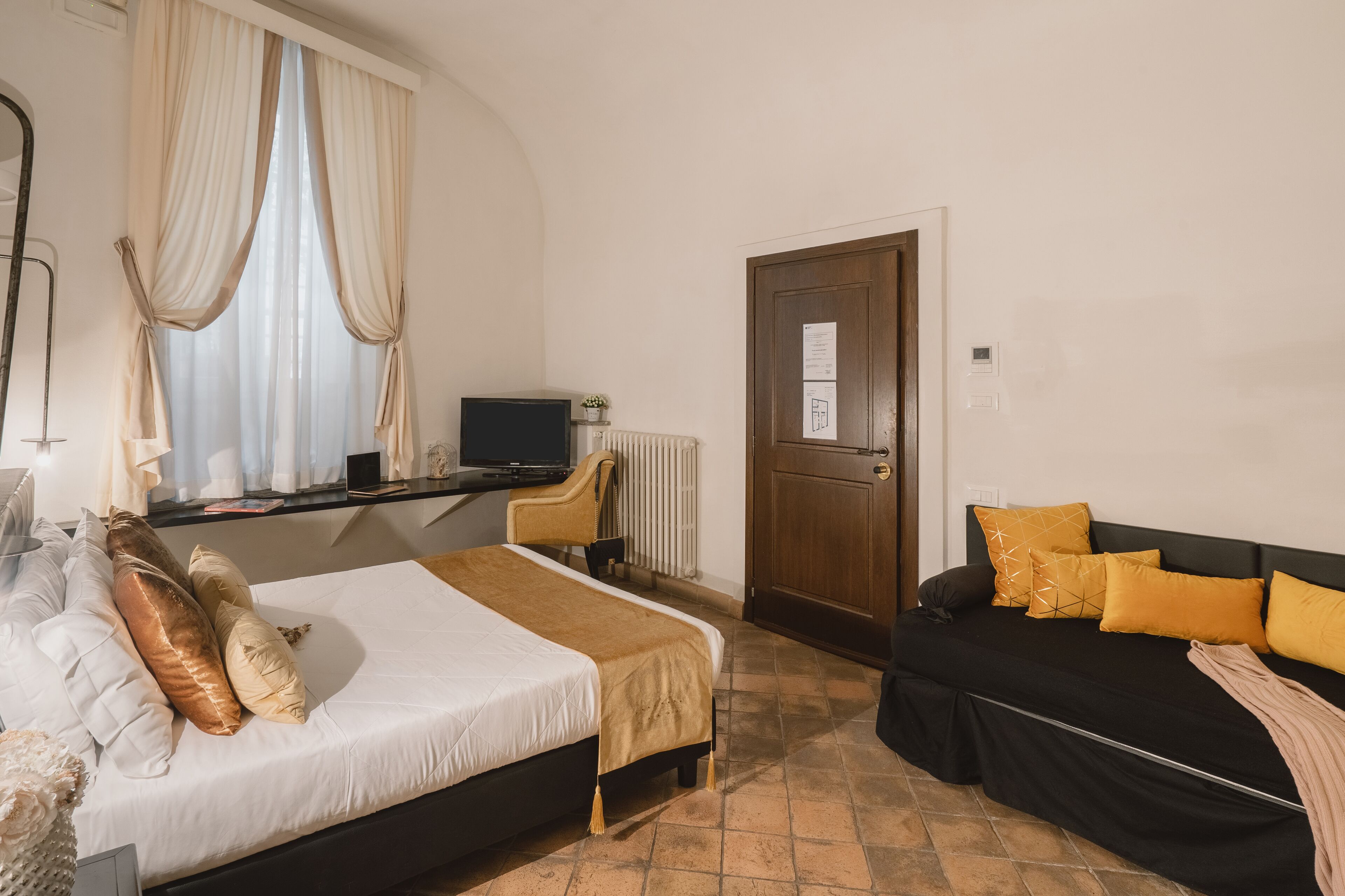 A hotel room with a bed, a sofa, a desk with a computer, and a door.