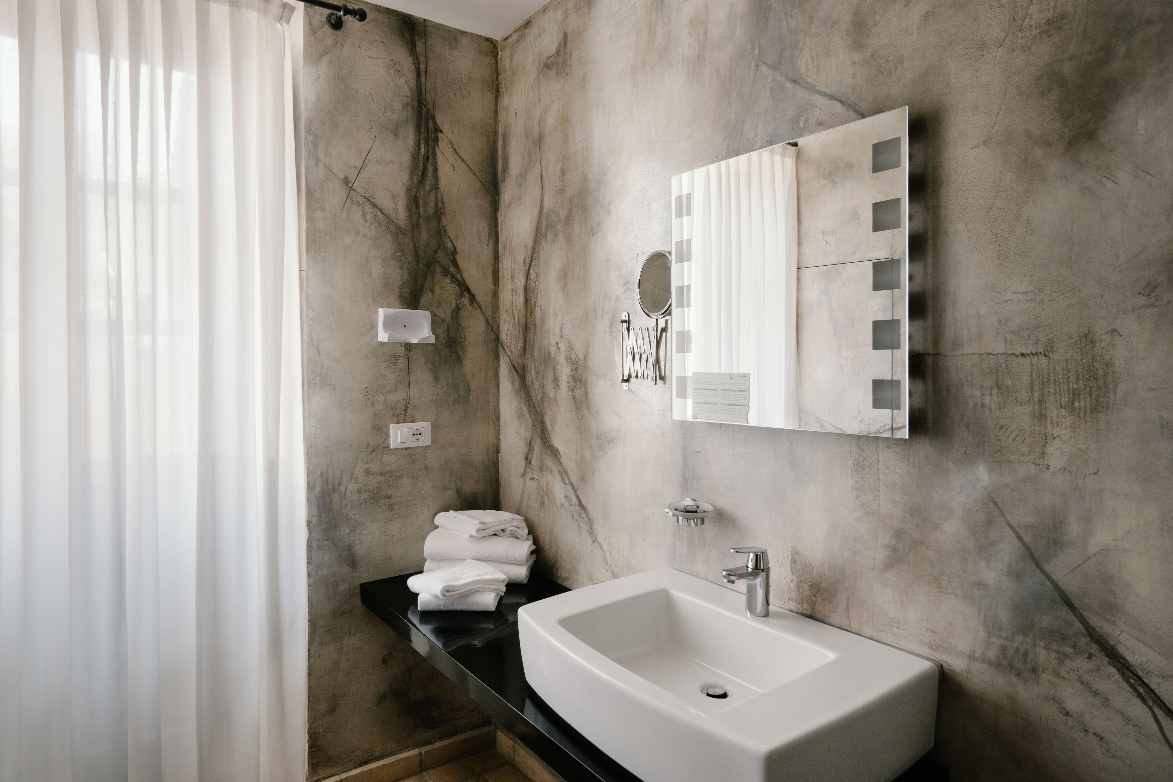 A modern bathroom with a marble wall, a white sink, and a vanity mirror.