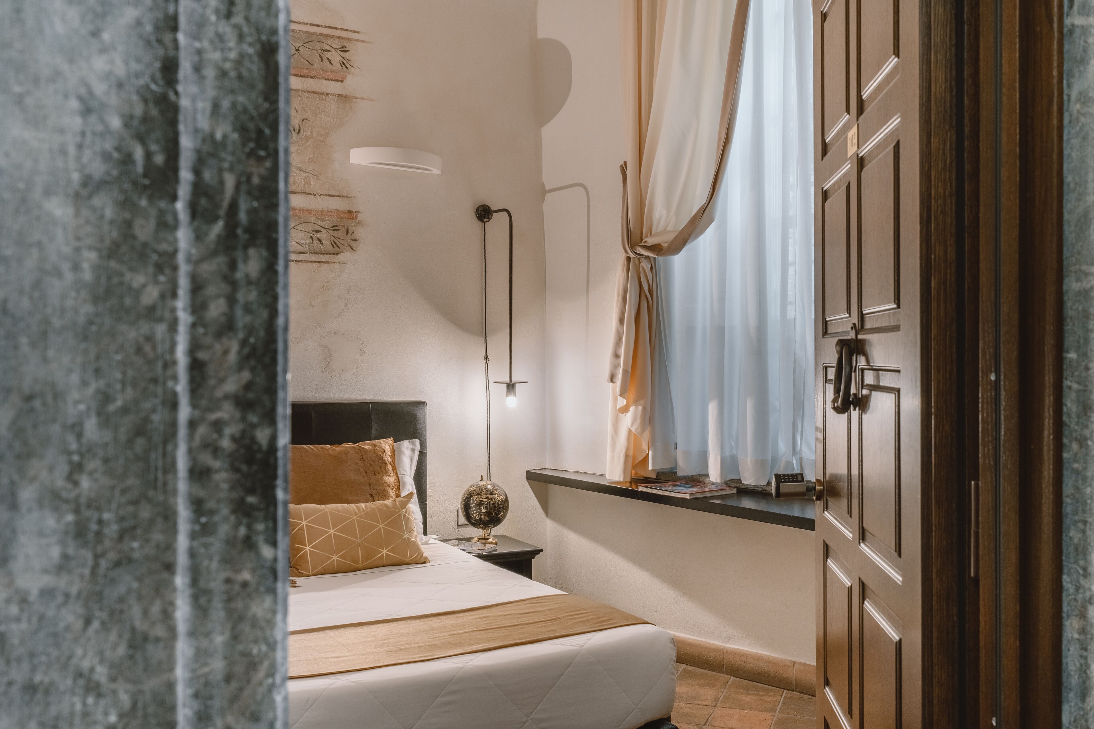 A bedroom with a bed, a nightstand, a lamp, a globe, and a window with curtains.