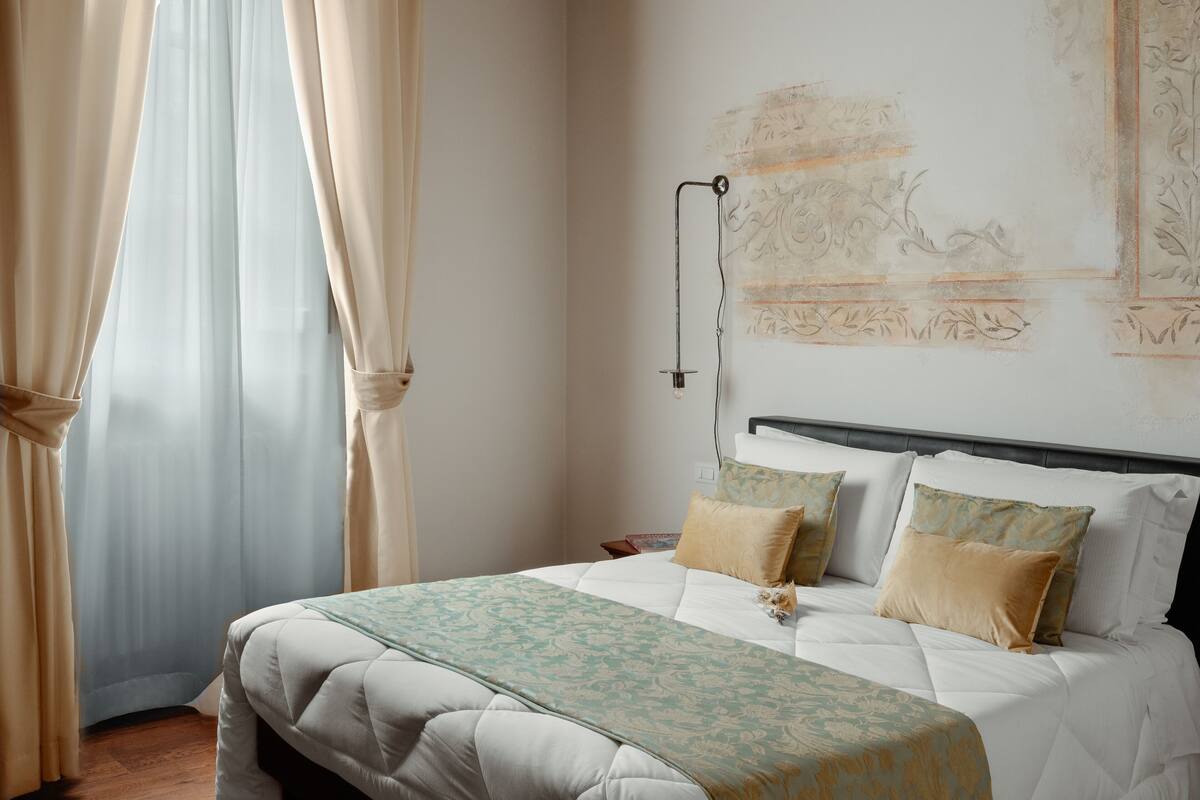 A bedroom with a bed, curtains, a wall-mounted light, and a decorative wall piece.