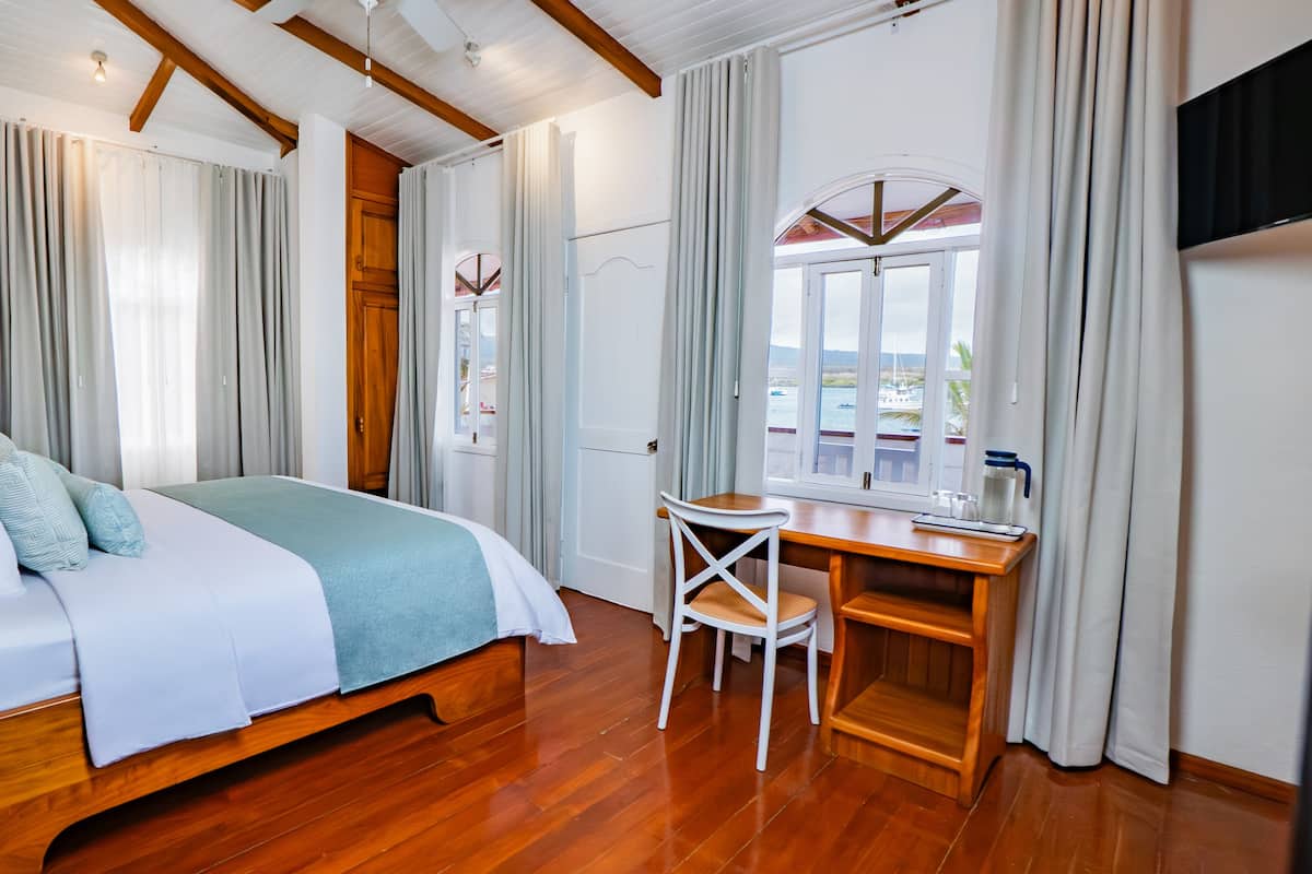 A bedroom with a bed, a desk, a chair, a window with a view, and a TV.