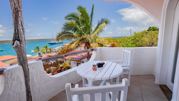 A balcony with a white table and chairs, overlooking a beach with boats and palm trees.