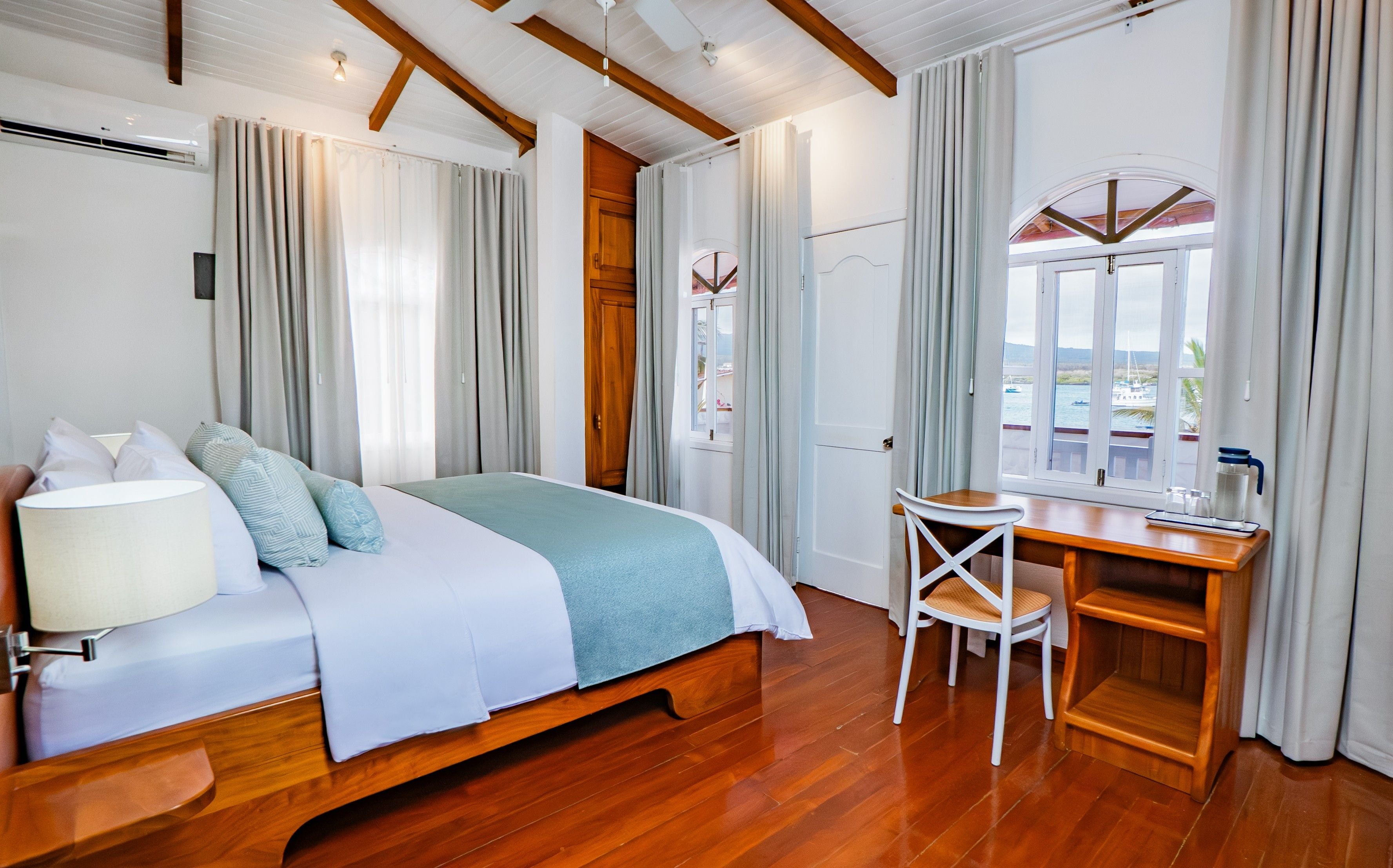 A bedroom with a bed, a desk, and a view of the sea.