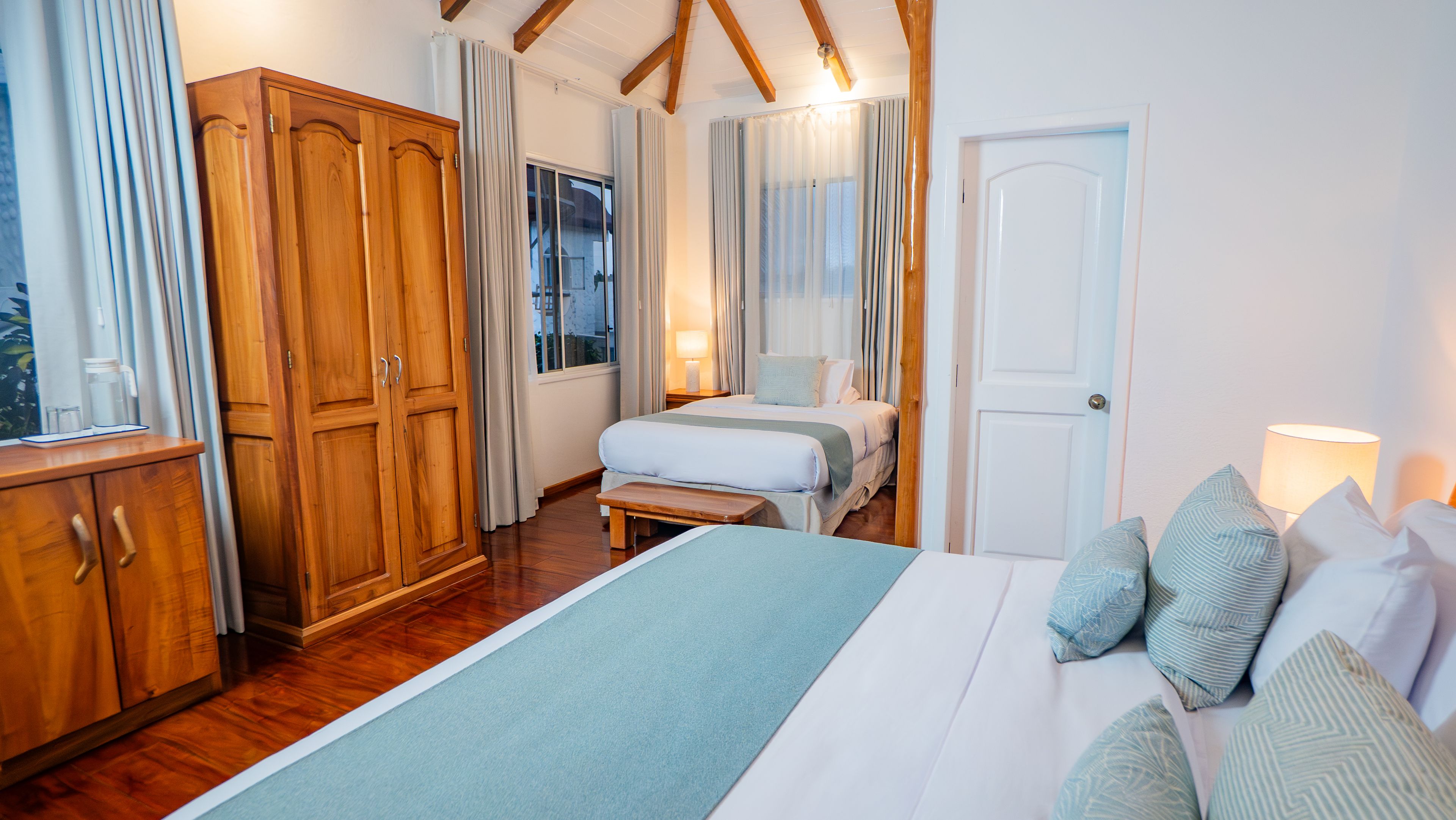 A bedroom with a large bed, wooden wardrobe, and a window with curtains.