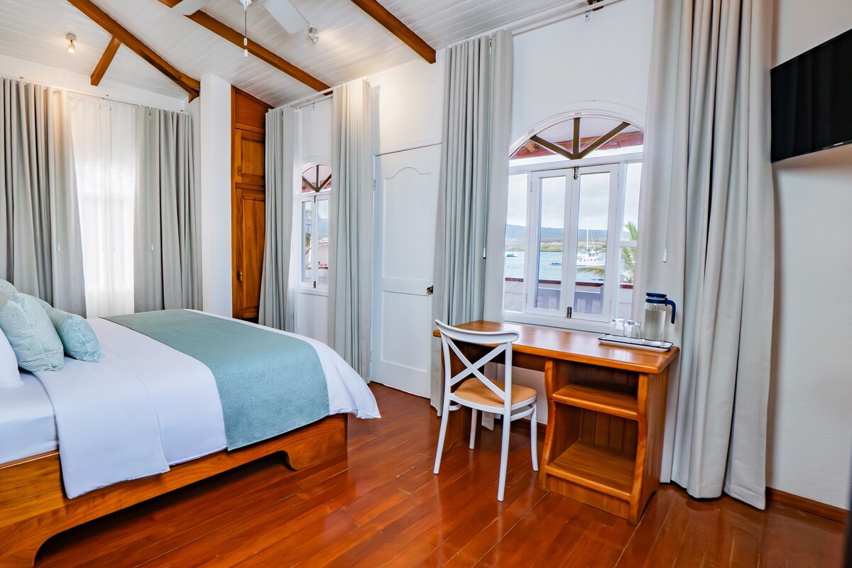 A bedroom with a bed, a desk, a chair, a window with a view, and a TV.