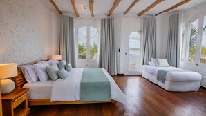 Una habitación de hotel con una cama, un sofá, suelo de madera y ventanas grandes con cortinas.