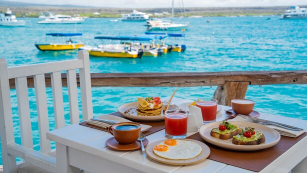 Una mesa de comedor con alimentos para el desayuno y vistas al mar con barcos.