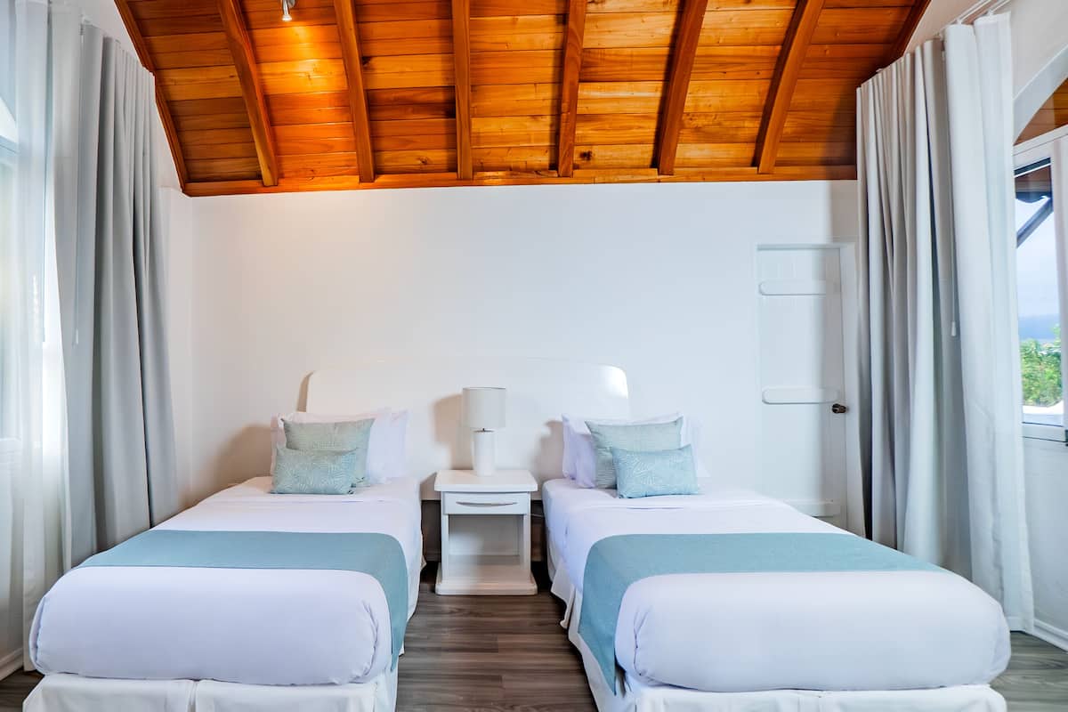 A room with two beds, a small table, and a ceiling with wooden beams.