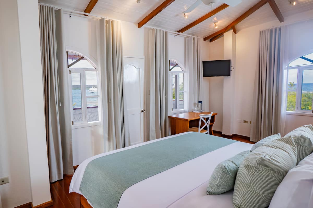 A bedroom with a bed, a desk, a chair, and a TV.