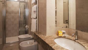 Et moderne badeværelse med bruseniche, toilet, bidet, vask og et stort spejl.