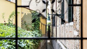 Un estrecho callejón flanqueado por edificios, una puerta metálica en primer plano y un camino adoquinado.