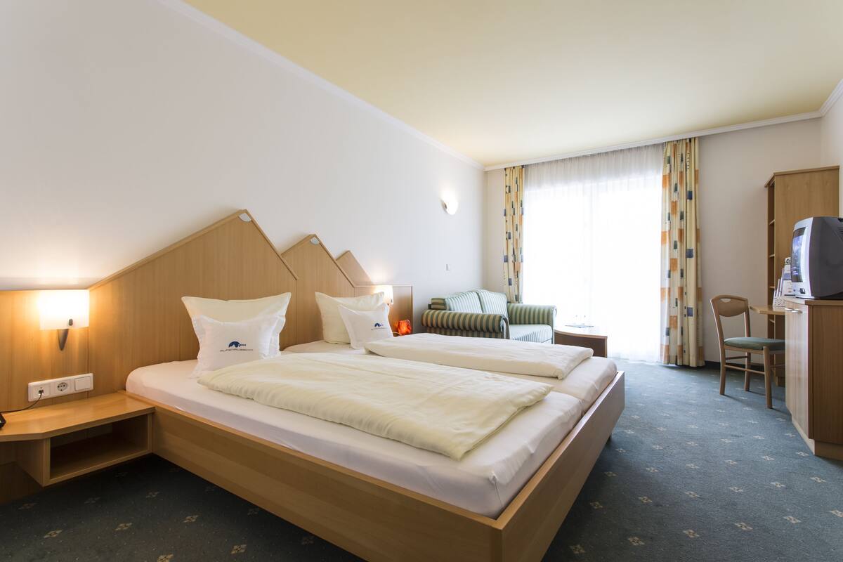 A hotel room with two beds, a desk, a chair, and a television.