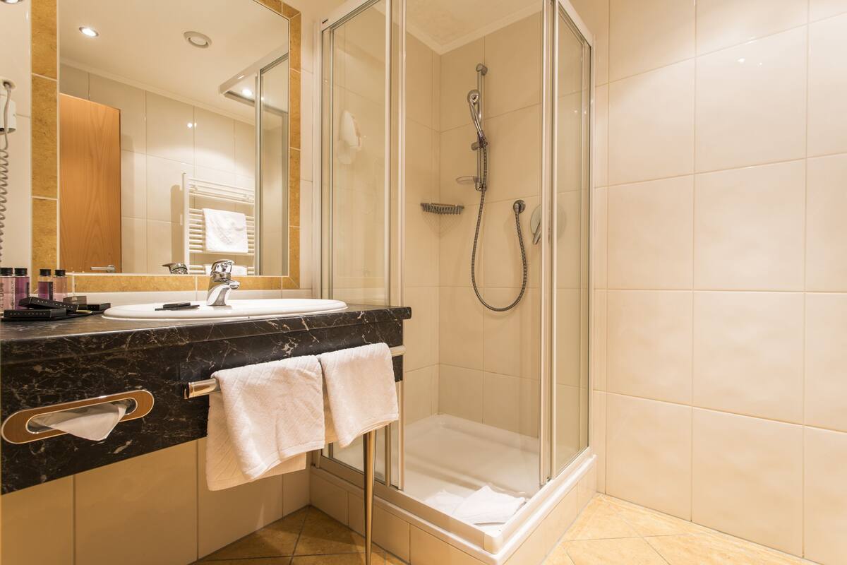 A modern bathroom with a glass-enclosed shower, a marble countertop, and a large mirror.