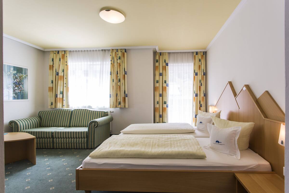 A hotel room with a bed, a sofa, a bedside table, and curtains.