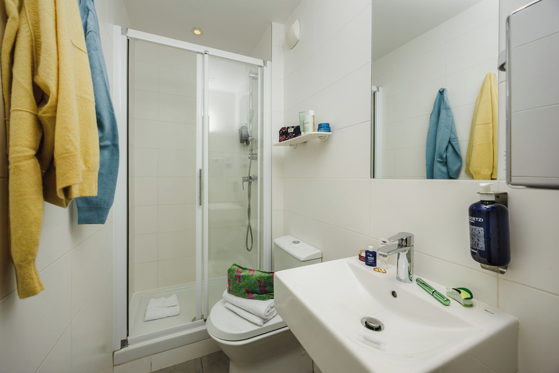 Une salle de bain avec une douche à parois de verre, des toilettes, un lavabo avec des articles de toilette et des serviettes accrochées au mur.