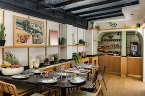 Un restaurant doté d’un long comptoir, de plusieurs tables et de chaises. Les murs sont décorés de plantes et d’œuvres d’art.