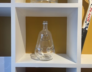 Una botella de vidrio transparente con una carita sonriente sobre una estantería.