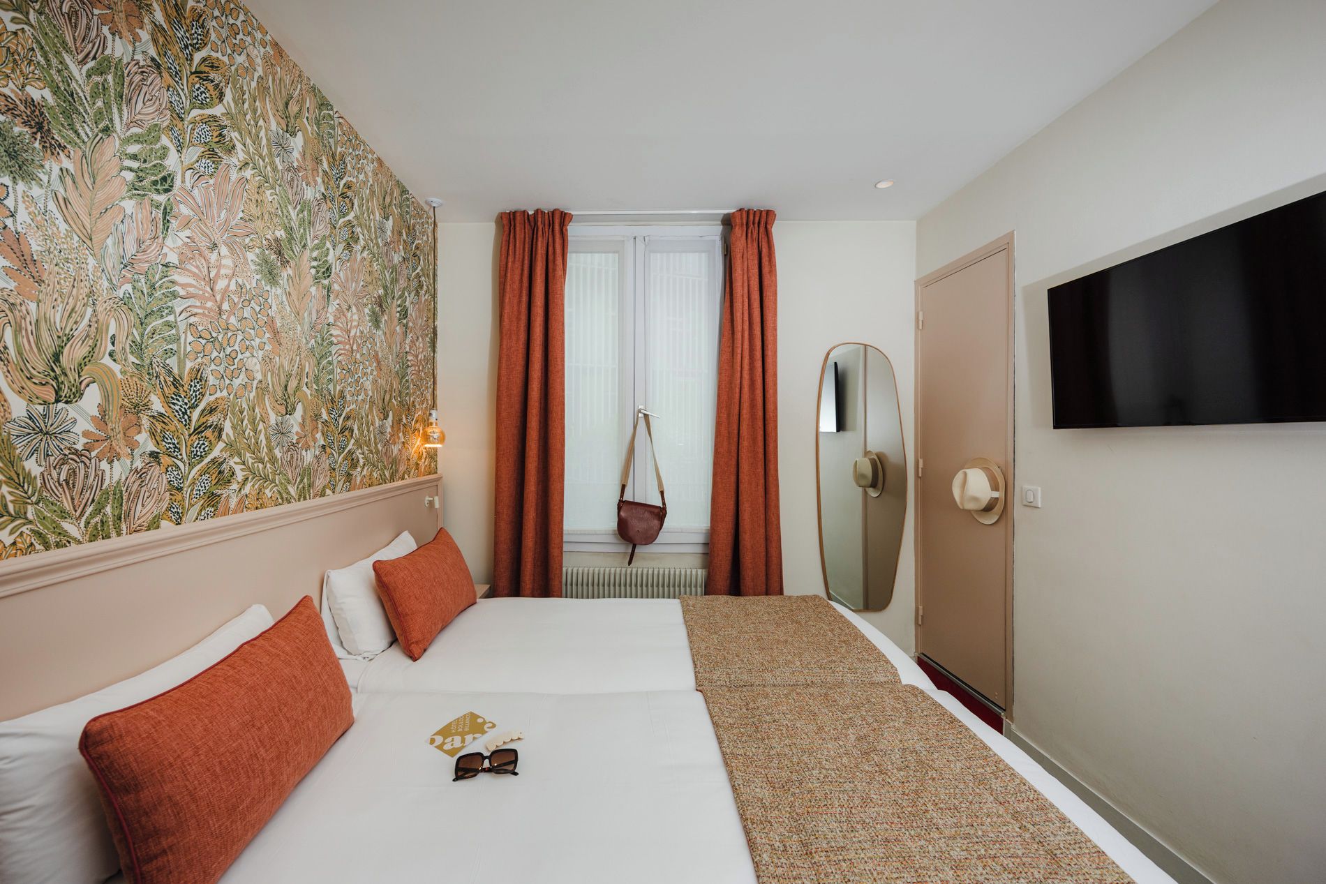Ein Hotelzimmer mit Bett, Spiegel, Fernseher und einem fenster mit Vorhängen.