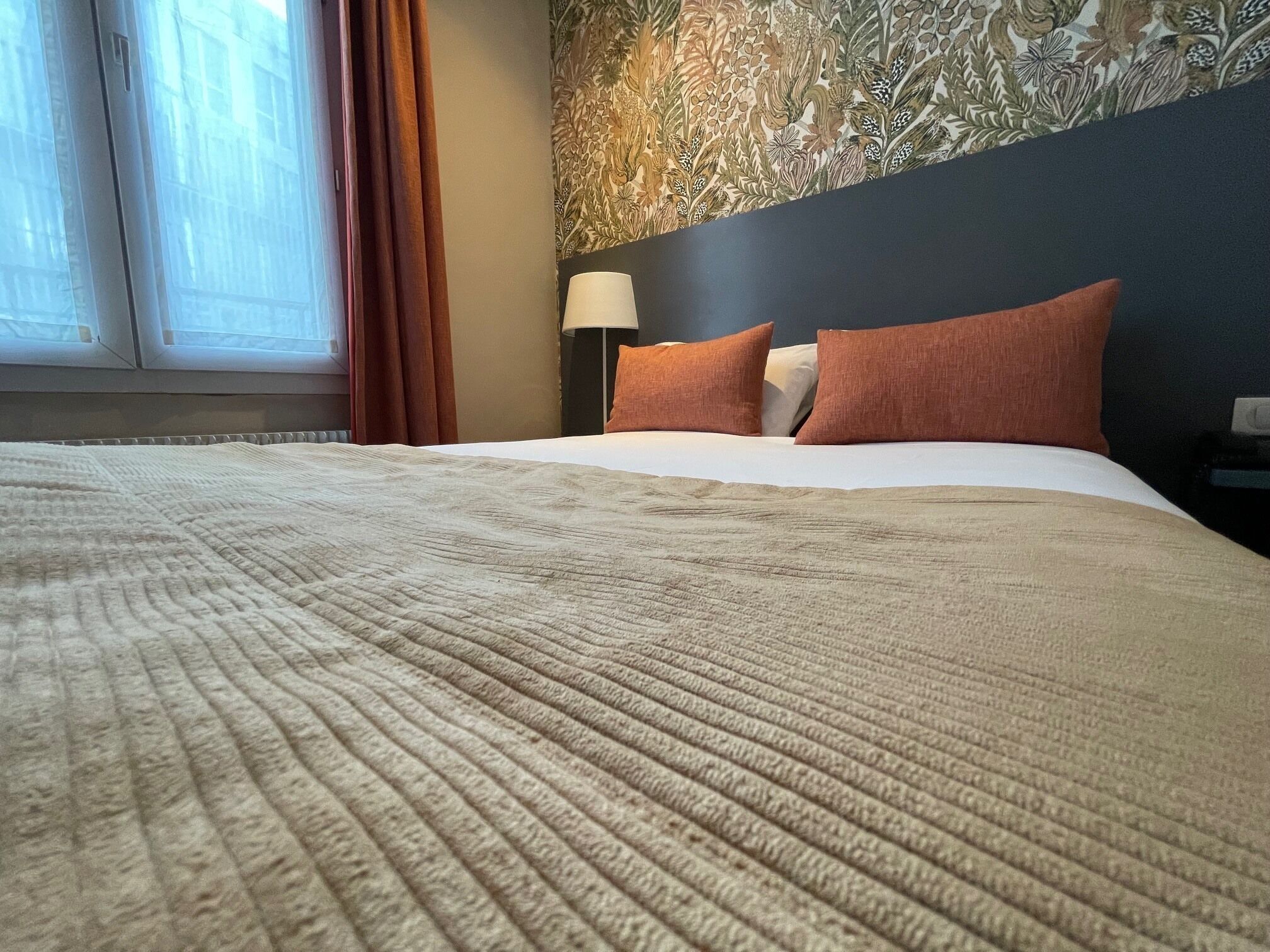Una habitación de hotel con una cama grande, una mesita de noche, una lámpara y una ventana con cortinas.