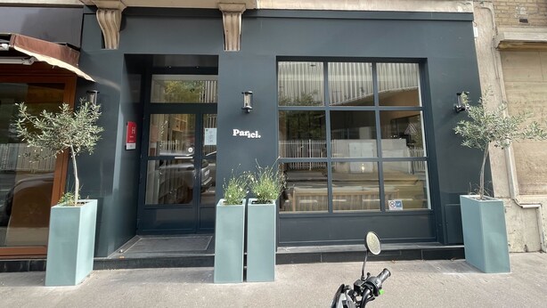 Un edificio con fachada negra, un letrero que dice "Parici" y dos plantas en macetas al frente.