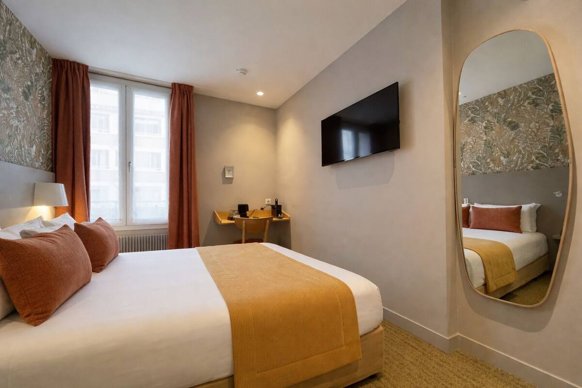 A hotel room with a bed, a desk, a flat-screen TV, a mirror, and a window with curtains.