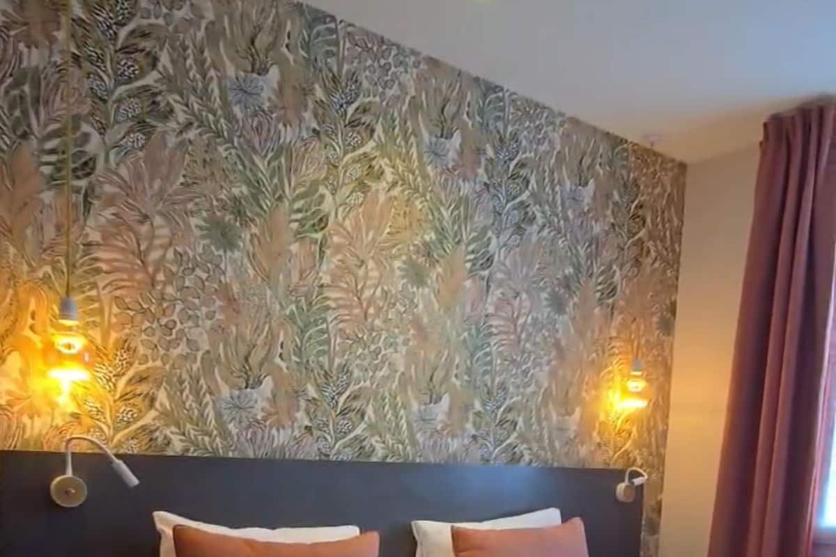 A hotel room with a large bed, two bedside tables, and a decorative wall with a leaf pattern.