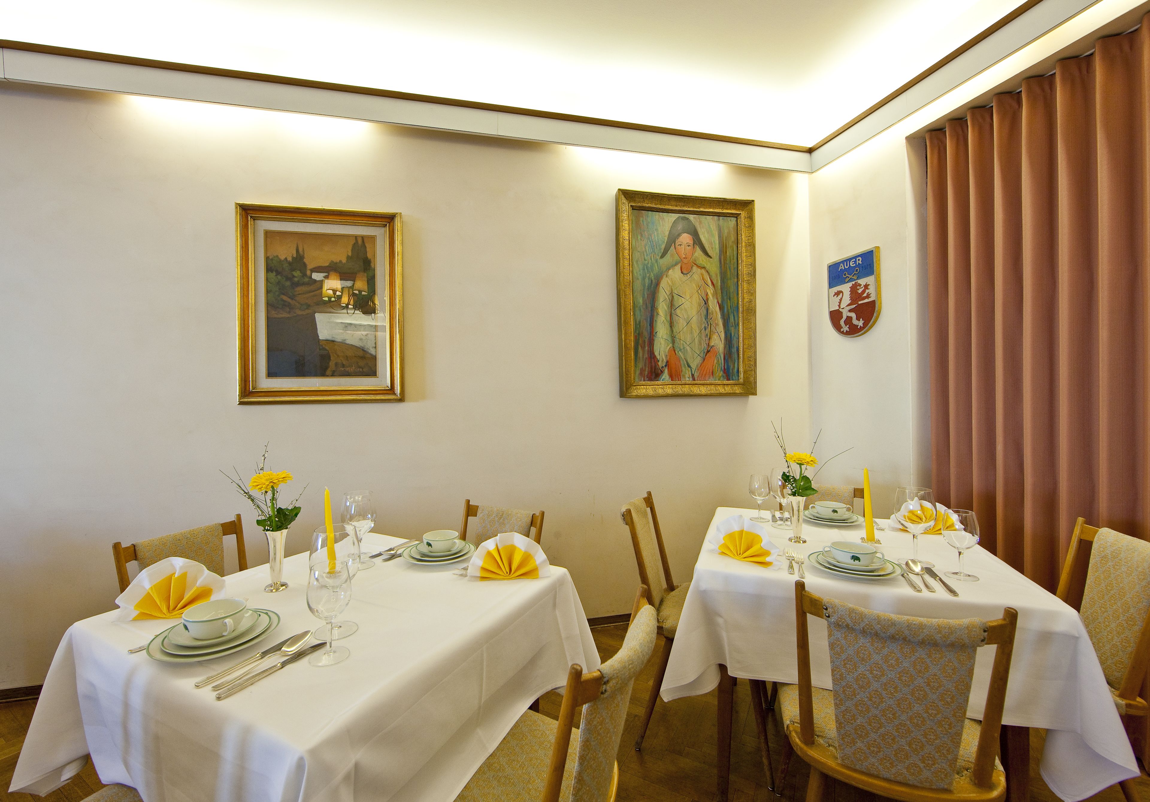 A dining room with two tables set for a meal, each with white tablecloths, yellow napkins, and silverware.