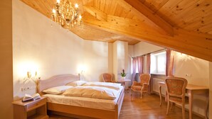 A bedroom with a wooden ceiling, a bed, a desk, and a chair. - Hotel Tyrol (Ora)