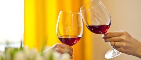 Two hands holding wine glasses with a yellow curtain in the background.