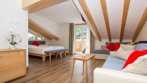 A modern loft-style room with a wooden ceiling, a sofa, a bed, a small table, and a view of greenery outside. - Hotel Tyrol (Ora)