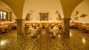 A dining area with tables and chairs, a tiled floor, and a high arched ceiling. - Hotel Tyrol (Ora)