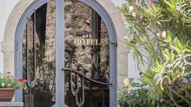 A hotel entrance with a large arched doorway, a metal gate, and a potted plant with flowers. - Hotel Tyrol (Ora)
