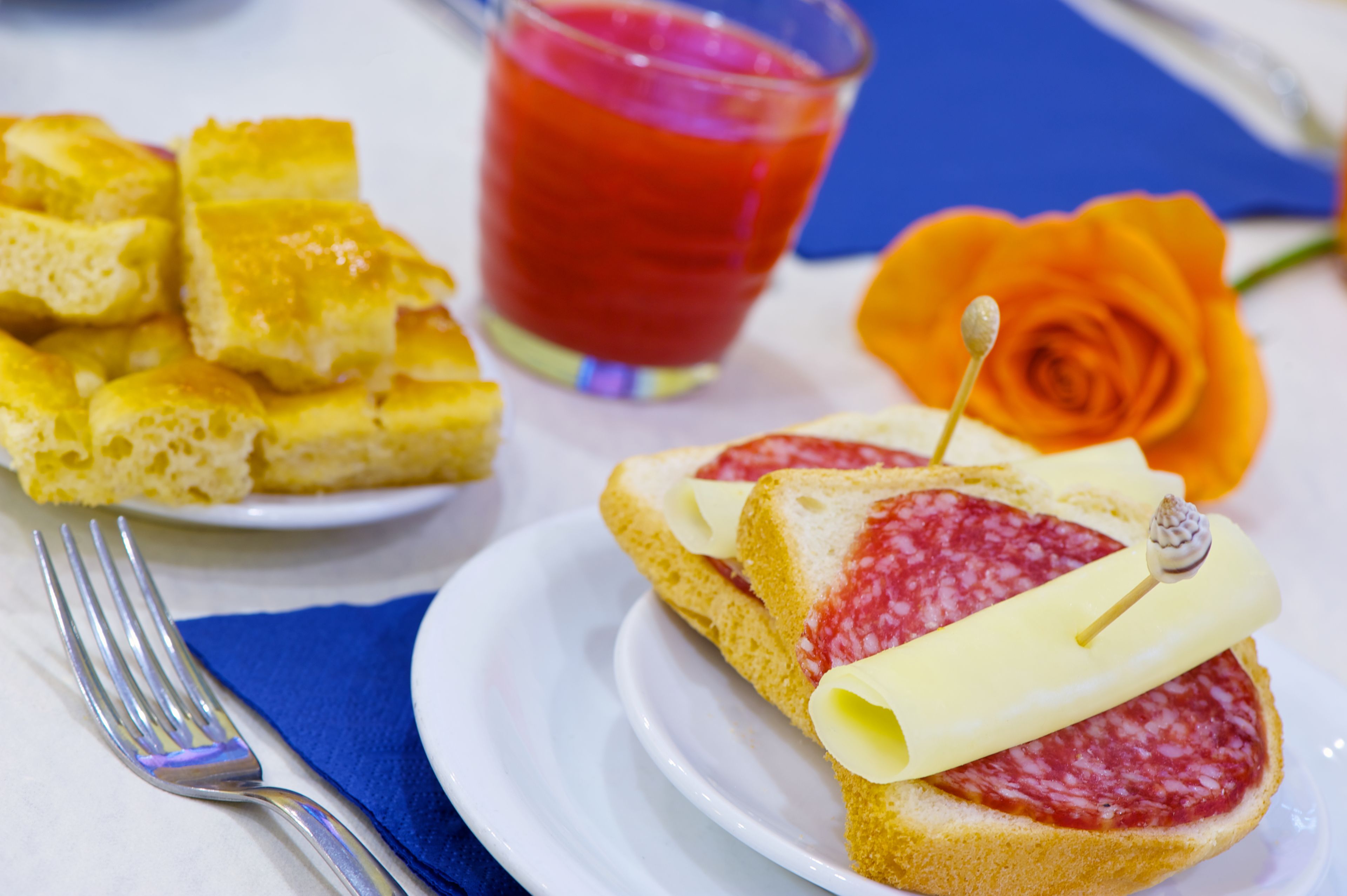 A plate of bread with cheese and salami, a glass of red drink, and a rose on a table.