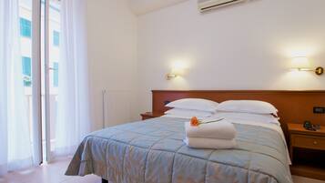 A hotel room with a bed, a nightstand, a lamp, and a view of the outside.