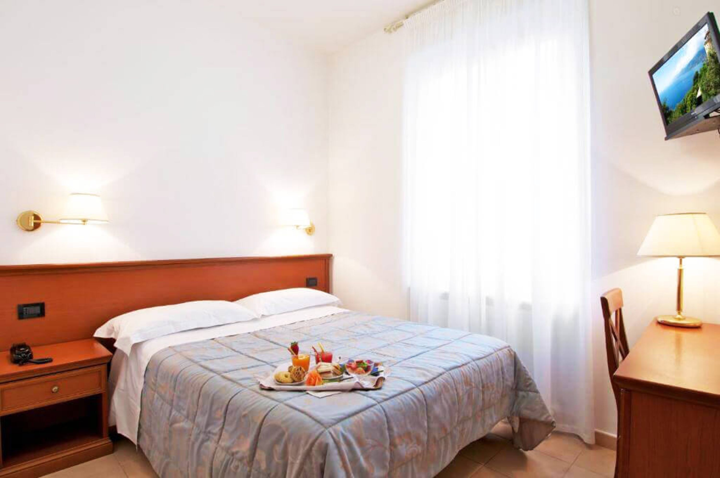 A hotel room with a bed, bedside table, TV, and a breakfast tray on the bed.