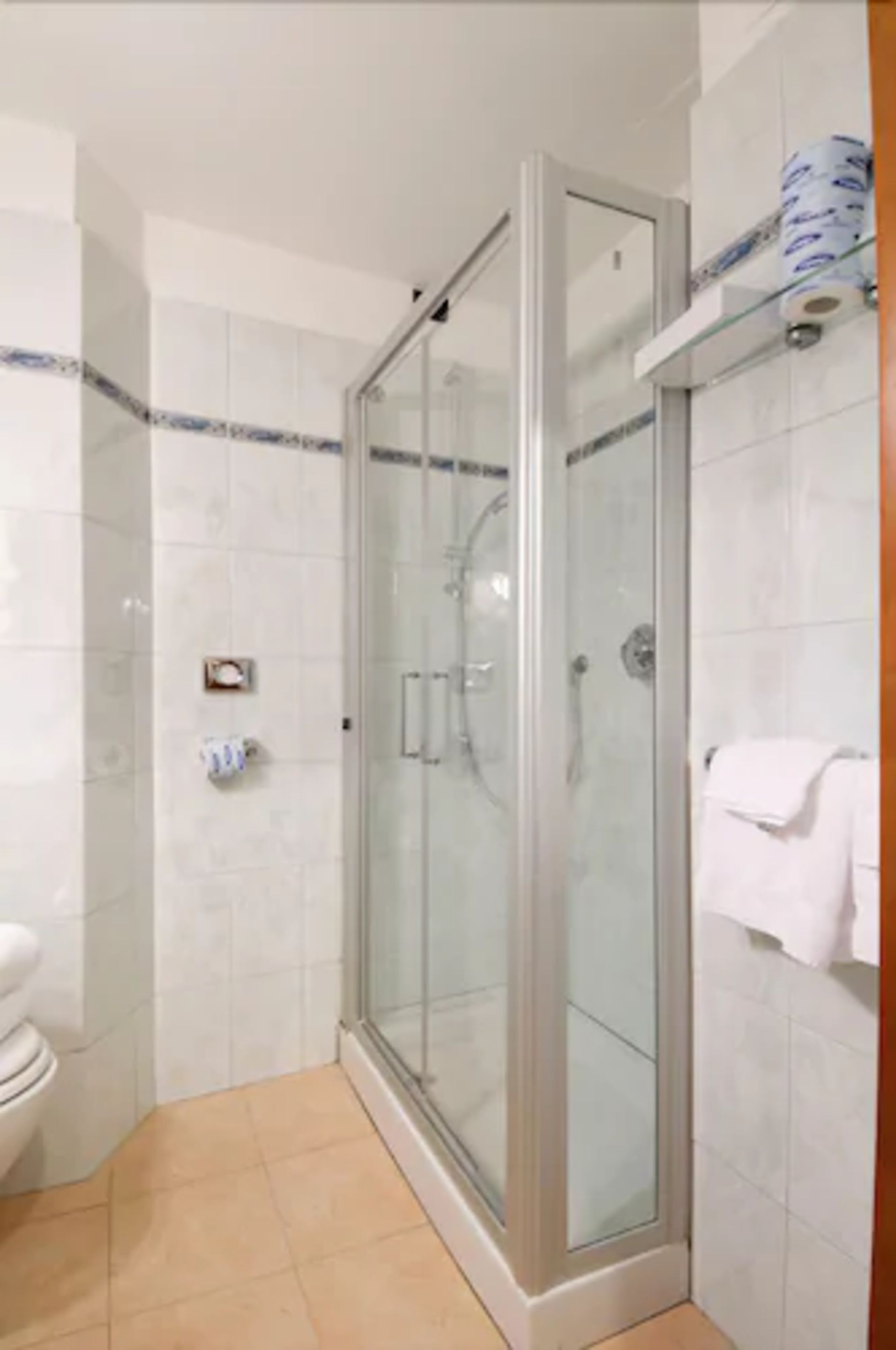 A glass-enclosed shower stall with a white tiled floor and a white towel hanging on a rack.