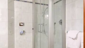 A glass-enclosed shower stall with a white tiled floor and a white towel hanging on a rack.