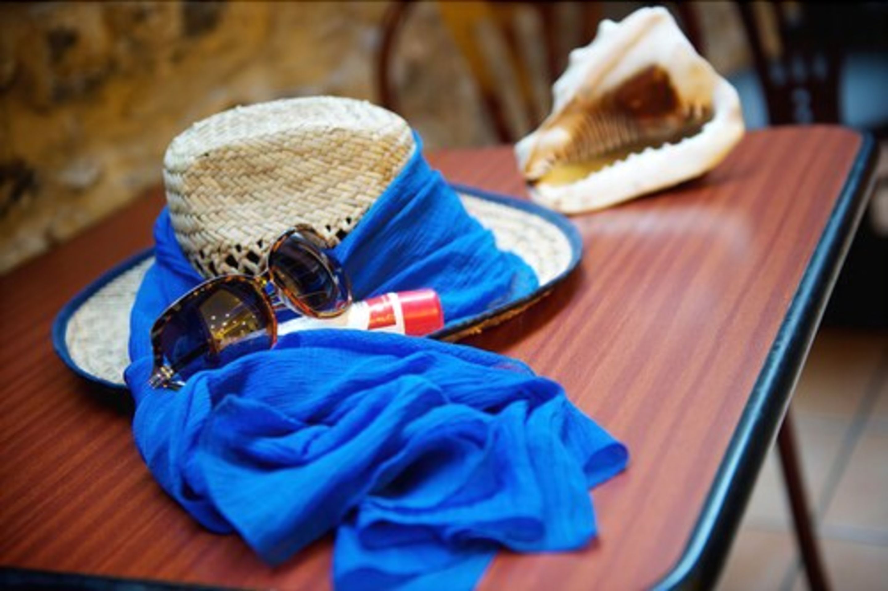 A straw hat, sunglasses, and a blue cloth on a wooden table.