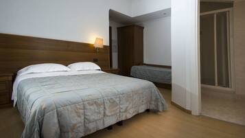 Un dormitorio con cabecera de madera, cama con colcha estampada, mesita de noche con lámpara y una puerta que da a otra habitación.