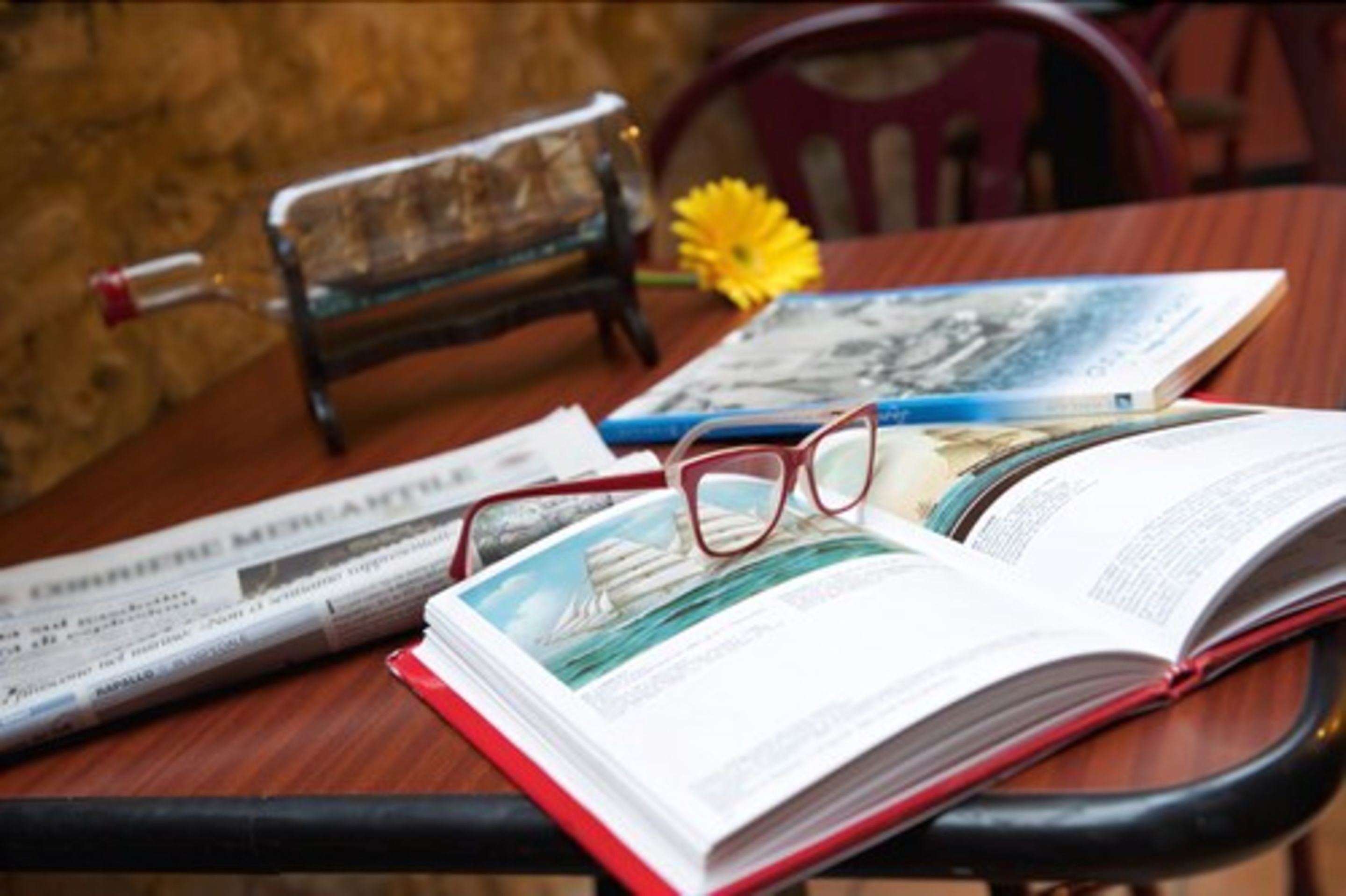 A book, glasses, and a newspaper on a wooden table.