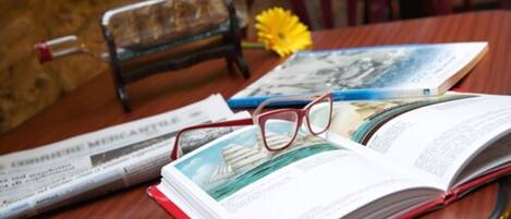 A book, glasses, and a newspaper on a wooden table.