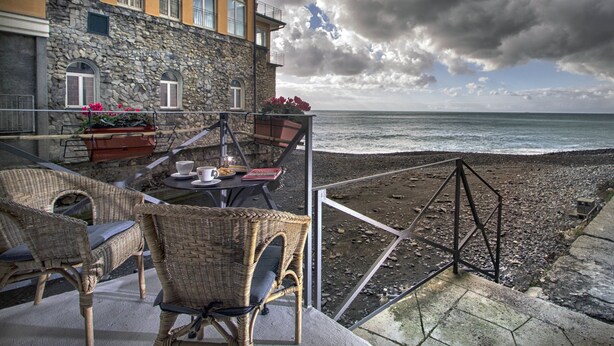 Een balkon met rieten meubels, een tafel met kop en schotel, en uitzicht op zee.